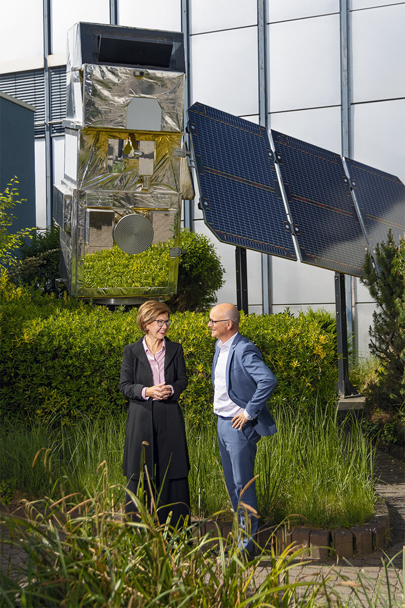 Zwei Mesnchen unterhalten sich fröhlich miteinander. Über ihren Köpfen ist ein Solarpanel zu sehen.