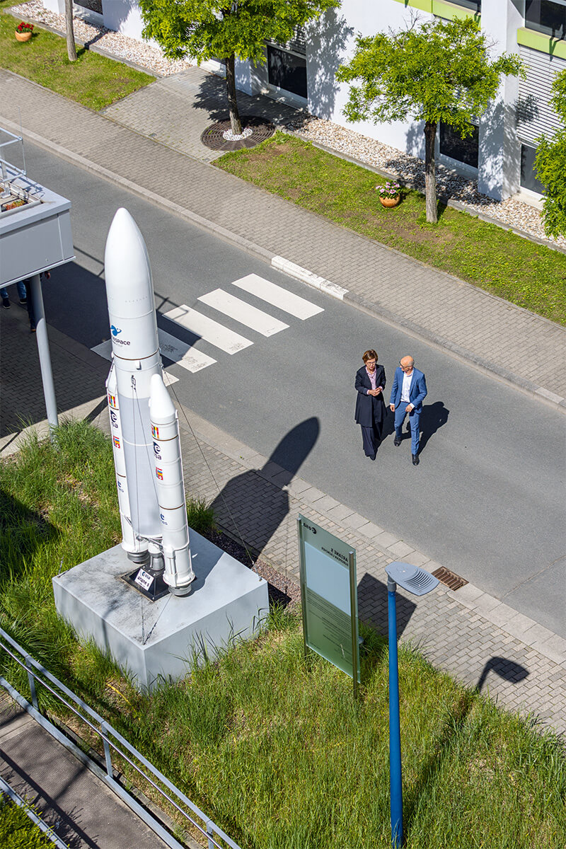 Zwei Menschen stehen auf einer Straße neben einem großen Modell einer Rakete.