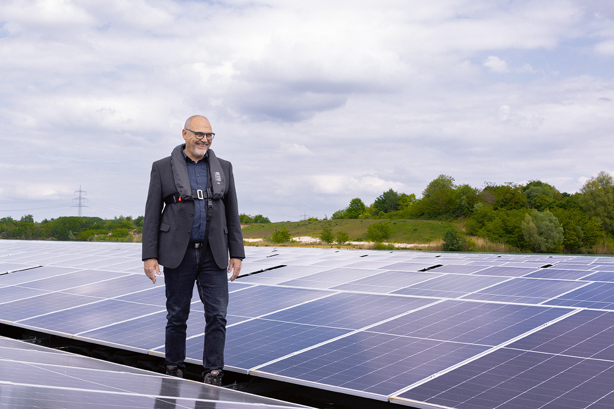 Person steht zwischen Photovoltaikmodulen in einem großen Solarpark.