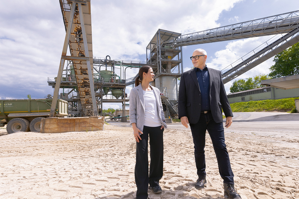 Julia Klinger und Andreas Niedermaier auf einem Industriegelände mit Förderanlagen..