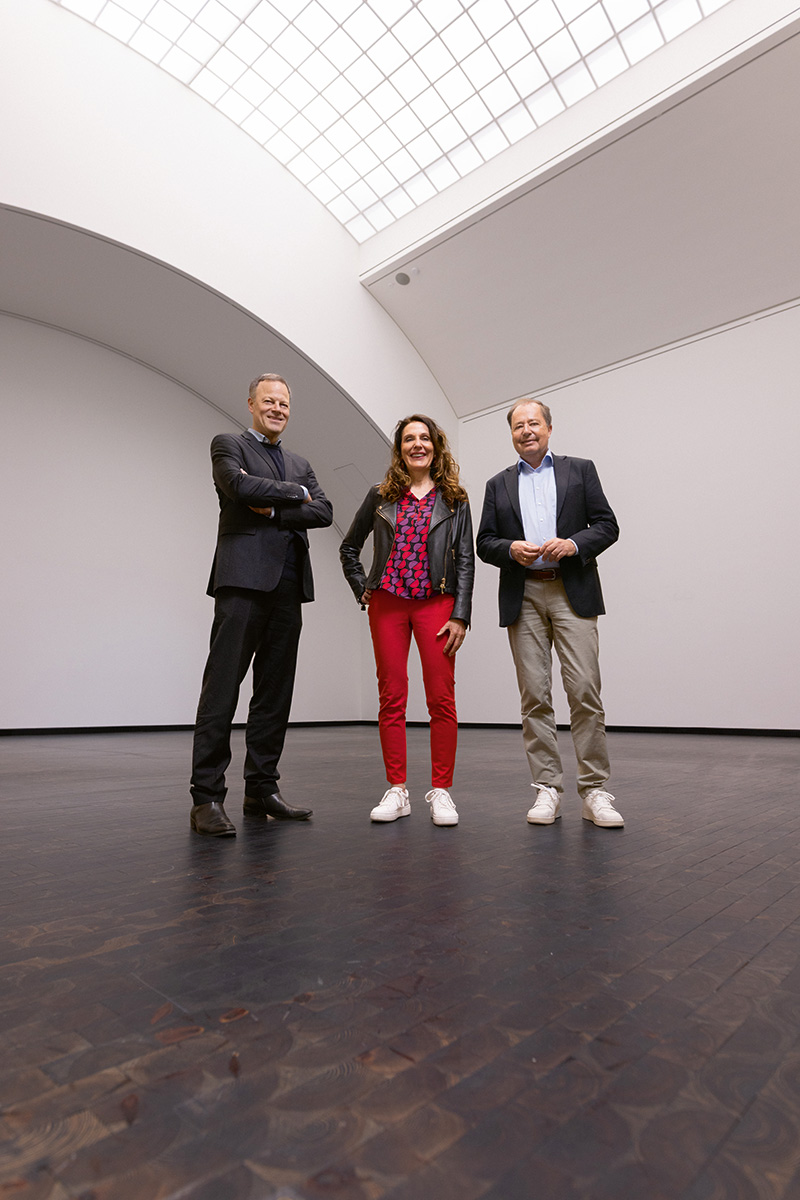 Anja Förster mit Dr. Philipp Gutbrod und Thomas Schmidt in einem hellen Ausstellungsraum mit Glasdach. Die Bestsellerautorin und Gründerin von Rebels at Work begleitet Führungskräfte durch Veränderung und beschäftigt sich mit der Wirtschaft von morgen.